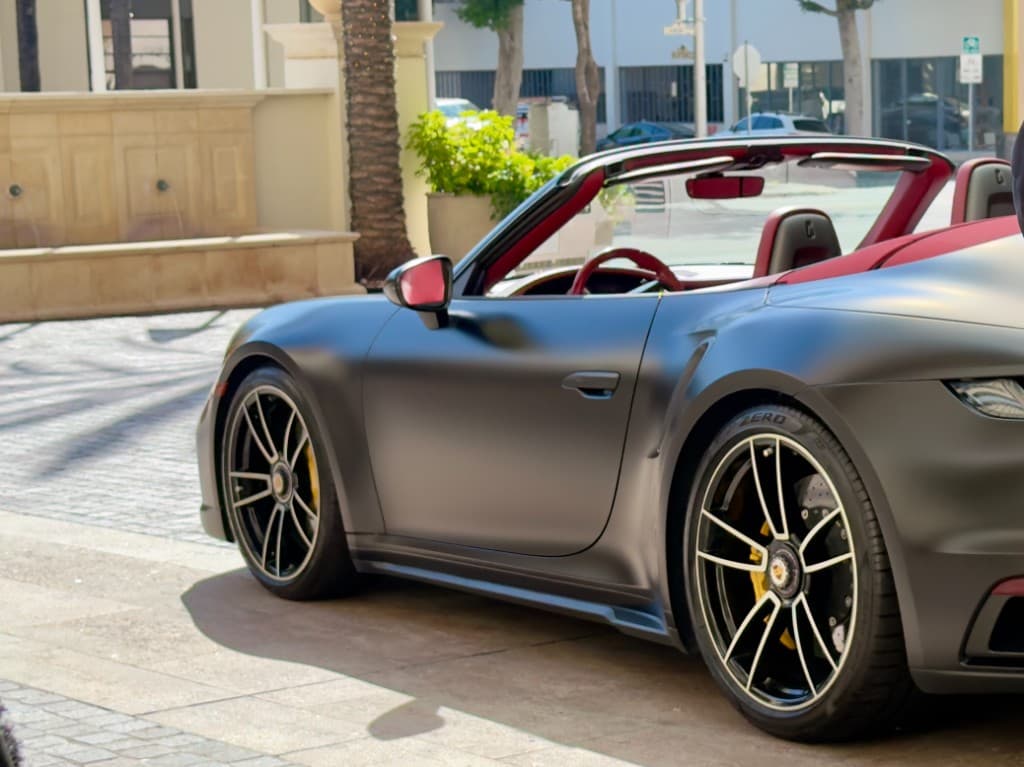 Porsche 911 Turbo S Cabriolet — matte black side profile on cobblestone, top down