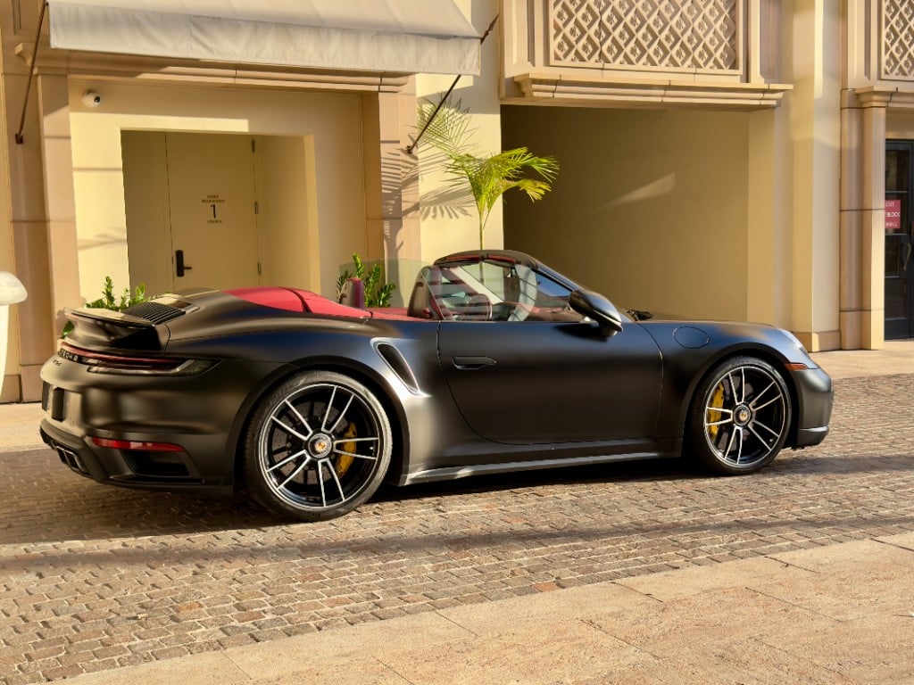 Porsche 911 Turbo S Cabriolet — matte black side profile with red interior at golden hour